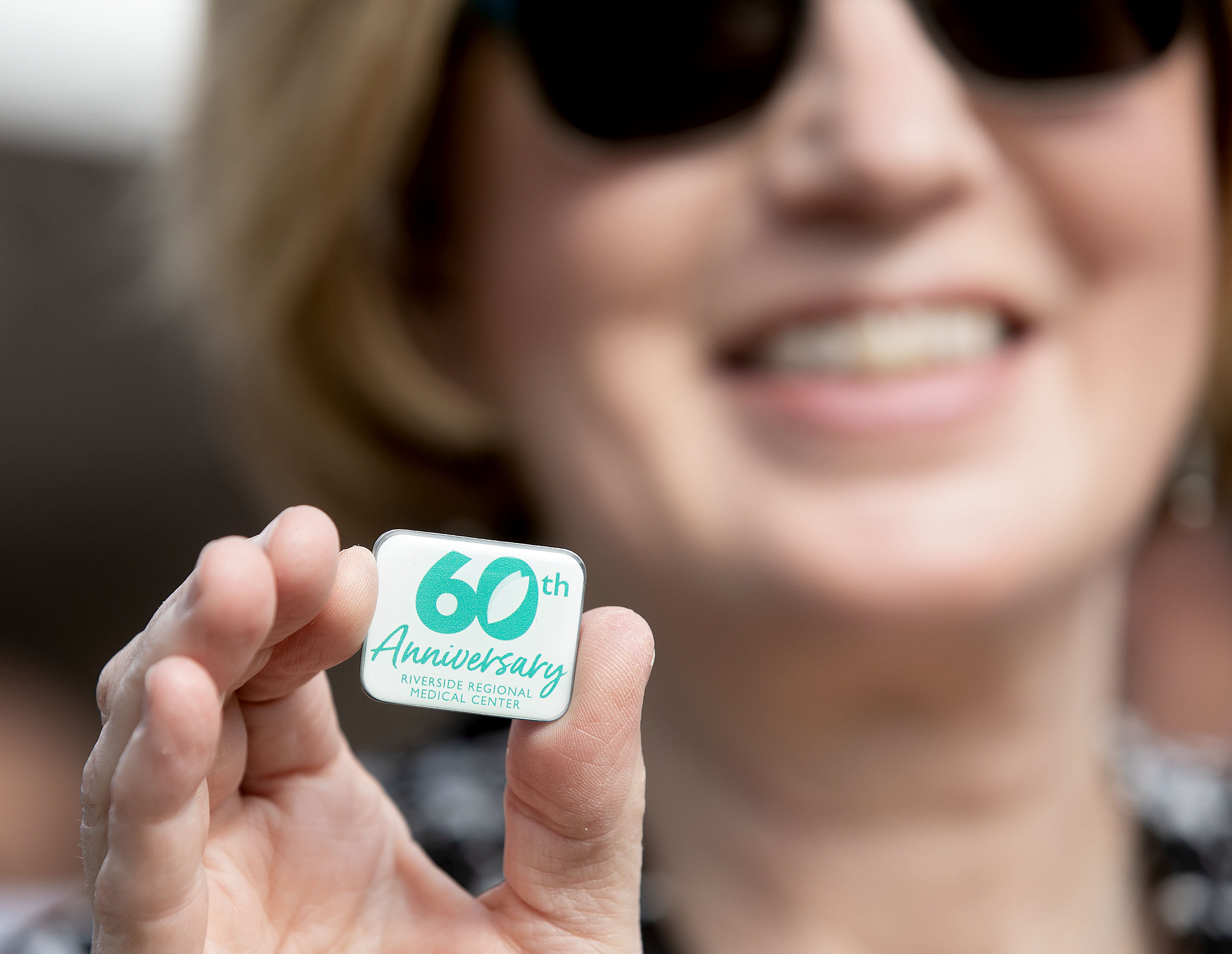 caucasian blonde woman holding small rectangular label pin with Riverside 60th anniversary written on it