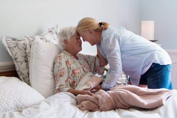 Adult daughter visits older mother sitting in bed