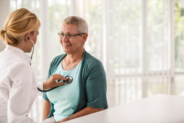 Female doctor listening senior woman's heartbeat during routine medical examination.