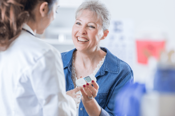 Smiling Caucasian female patient discusses diabetes with her doctor during medical appointment.